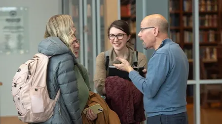 Professor talking to three college students in academic building