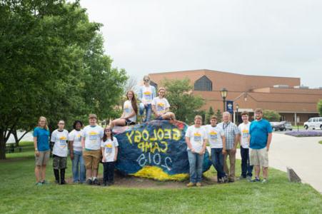 Students pose for a picture around a large rock